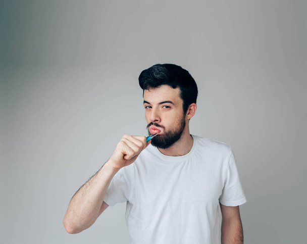Young man isolated over background. Cleaning teeth with toothbrush. Healthcare and oral treatment. Posing on camera. Alone in studio. Dental care. - Foto, Bild