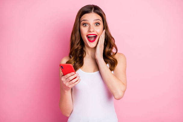 Portrait of excited astonished girl use smart phone get social network like notification impressed scream wow omg wear stylish singlet isolated over pink color background - Fotó, kép