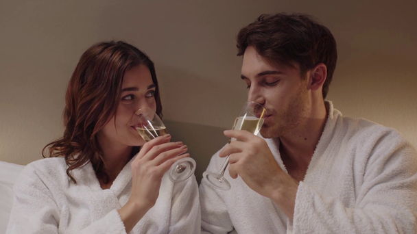 feliz pareja en albornoces tintineo vasos con champán en la habitación del hotel
 - Metraje, vídeo