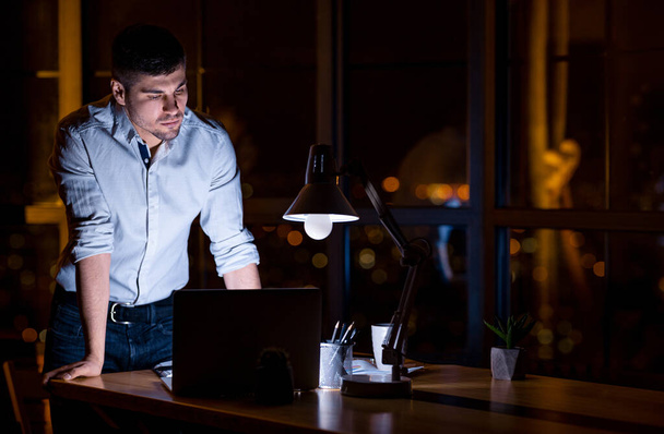 Empresário trabalhando no laptop de pé no escritório tarde da noite
 - Foto, Imagem