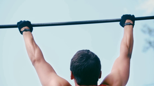 back view of sportsman in red tank top doing pull ups on horizontal bar - Кадры, видео