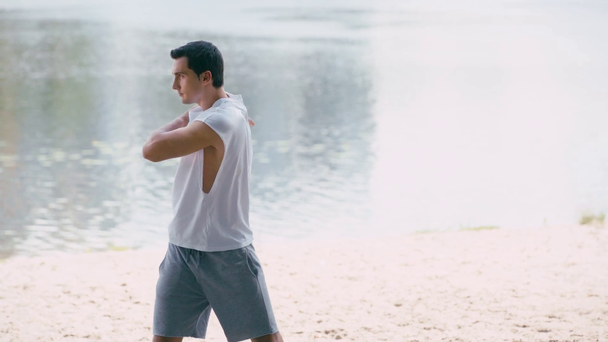 jong sportman opwarmen terwijl het doen van lichaam rotatie op zand kust - Video