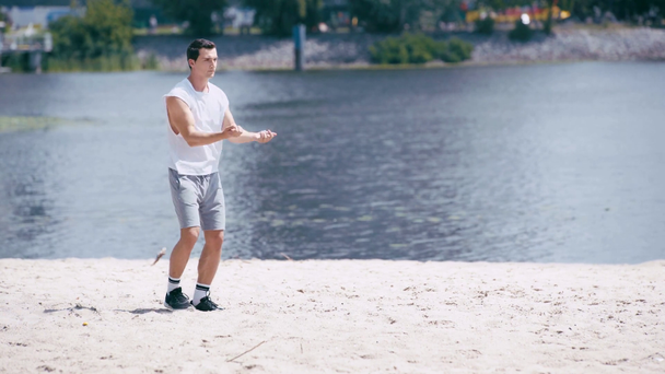 młody sportowiec w koszulce i spodenki rozgrzewające się na brzegu rzeki  - Materiał filmowy, wideo