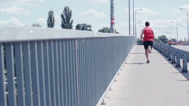 back view of young sportsman running over bridge - Кадри, відео