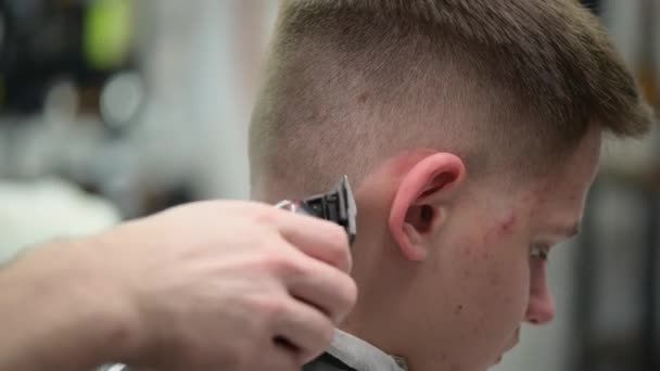 Egy fiatal férfi hajvágása a fodrászatban. Közelkép a mester nyírás haj csipeszrel a tarkóján - Felvétel, videó