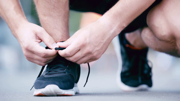 обрезанный вид спортсмена завязывающего шнурки на кроссовках
 - Кадры, видео