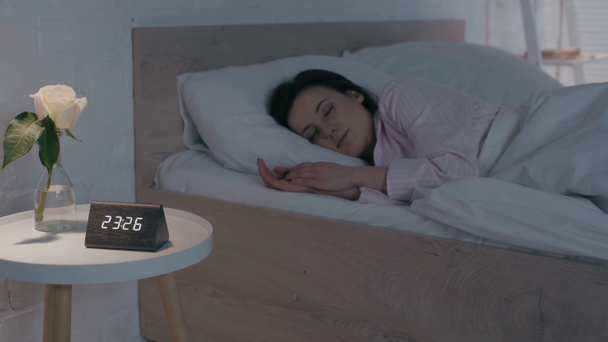 Ελκυστική γυναίκα κοιμάται στο κρεβάτι κοντά σε τριαντάφυλλο και ρολόι στο κομοδίνο  - Πλάνα, βίντεο