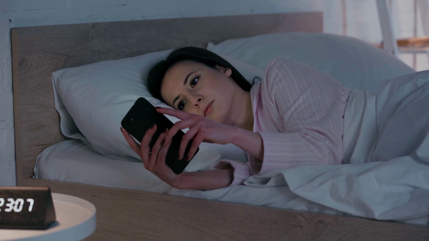 Nainen, joka käyttää älypuhelinta sängyssä yöllä - Materiaali, video