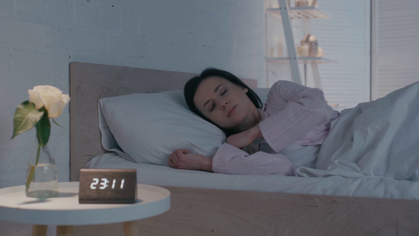 Selektiver Fokus einer an Schlaflosigkeit leidenden Frau nahe der Uhr auf dem Tisch  - Filmmaterial, Video
