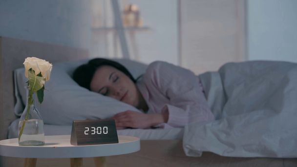 夜寝ている女性の近くのテーブルの上の時計と花の選択的な焦点  - 映像、動画