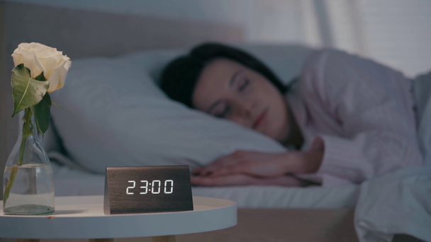 時計の選択的な焦点と夜にベッドで寝ている女性の近くのテーブルの上に上昇 - 映像、動画