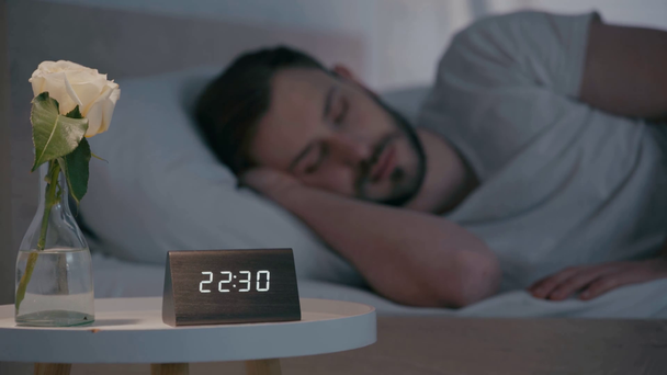 夜にベッドで寝ている男の近くのテーブルの上に時計とバラの選択的な焦点 - 映像、動画