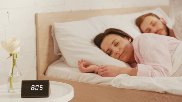 Selective focus of young couple sleeping on bed near clock and rose on table - Séquence, vidéo