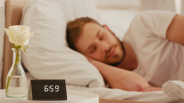 時計の選択的な焦点は、ベッドサイドテーブルの上に上昇し、男は朝に寝て  - 映像、動画