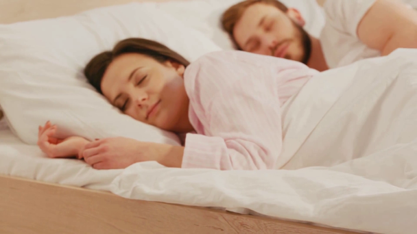 午前中にベッドで寝ているカップルの近くのテーブルの上の時計の選択的な焦点  - 映像、動画