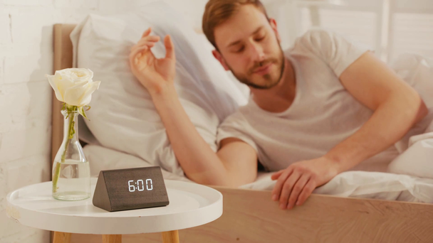 Selectieve focus van wekker en steeg op tafel in de buurt van de man wakker op bed - Video