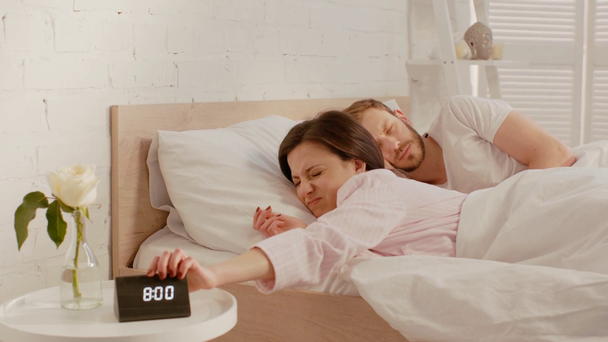 Woman turning off alarm clock while sleeping near boyfriend on bed  - Footage, Video