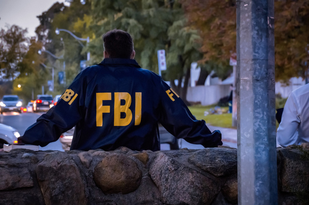 FBIのロゴ入りダークブルーのコートを着た男性FBI捜査官後ろから見た夕暮れ時に車で通りを見下ろします - 写真・画像