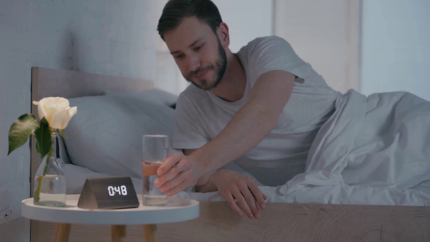 Selective focus of man drinking water near sleeping woman in bed at night - Imágenes, Vídeo