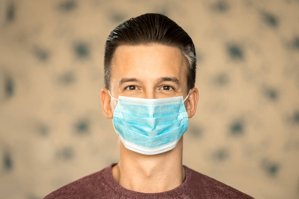 A koronavírus és a biztonság témája. Egy fiatal férfi kék maszkban, egy vírus mosolyától.. - Fotó, kép
