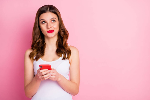Portrait of inspired positive girl use cellphone look copyspace think thoughts dream dreamy what post on social network account wear white singlet isolated over pink color background - Photo, image
