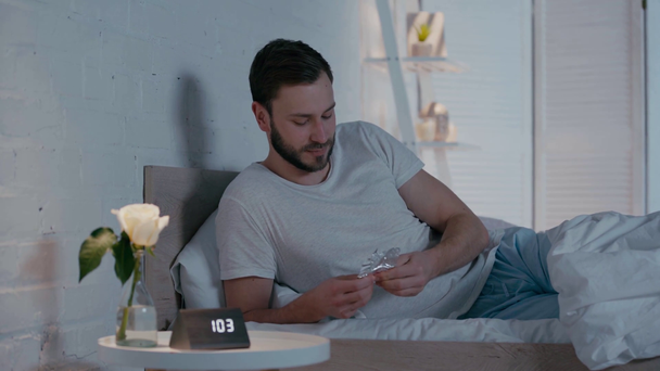 Smiling man eating chocolate on bed near sleeping girlfriend at night - Filmmaterial, Video