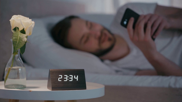 Επιλεκτική εστίαση του χαμογελαστού ανθρώπου χρησιμοποιώντας smartphone στο κρεβάτι τη νύχτα  - Πλάνα, βίντεο