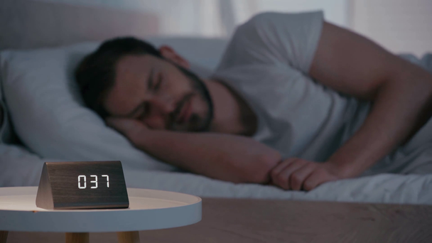 Selective focus of man suffering from insomnia near clock on bedside table - Footage, Video