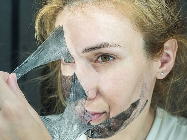Meisje scheurt zwart dun transparant masker om poriën schoon te maken - Foto, afbeelding