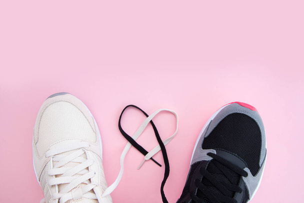 Männliche und weibliche weiße und schwarze Turnschuhe und Schnürsenkel in Herzform auf rosa Hintergrund. Fitness für sie und für ihn. Sportliebhaber. Heimtraining. Kopierraum - Foto, Bild