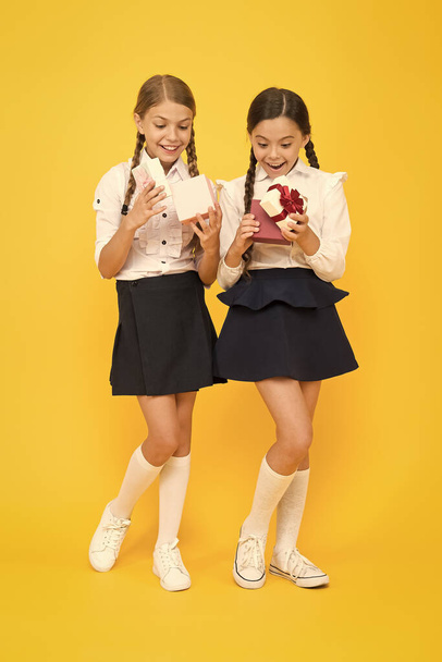 Rewarding excellent pupils. Girls opening gifts yellow background. Classmates tidy pupils open gifts boxes. Educational program for gifted kids. Best pupils award. Holiday celebration. Sharing gifts - 写真・画像