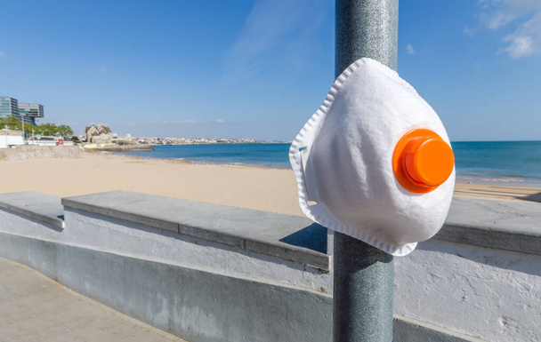 Mascarilla protectora en el poste con vistas a una playa pública vacía durante el brote de Coronavirus
. - Foto, Imagen