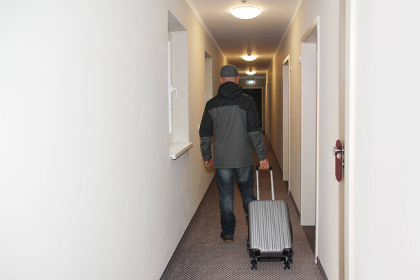 adult man goes down the hotel corridor to his room with a suitcase and keys in his hand, the concept of a long-awaited vacation, business trip - Valokuva, kuva