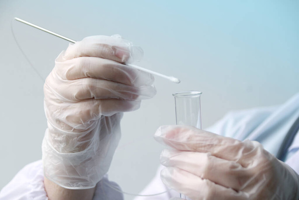 laboratory assistant in gloves puts a sample for DNA analysis on a cotton swab into a glass test tube, a scientific, police investigation and medical examination concept, close-up - Foto, Imagen