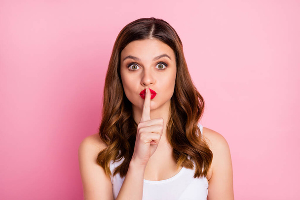Hush dont tell anyone. Astonished ginger hair girl know incredible gossip impressed put mute sign index finger mouth ask keep secret wear good look tank-top isolated pink color background - Foto, imagen