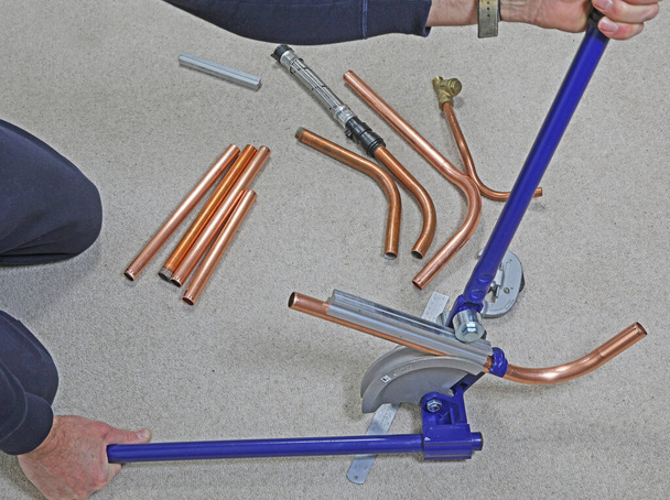 Un homme utilisant une plieuse de tuyaux pour créer un virage dans un tuyau en cuivre
. - Photo, image
