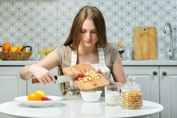 Молодая красивая женщина с фруктами на кухне, женщина сидит за столом и режет яблоки
 - Фото, изображение