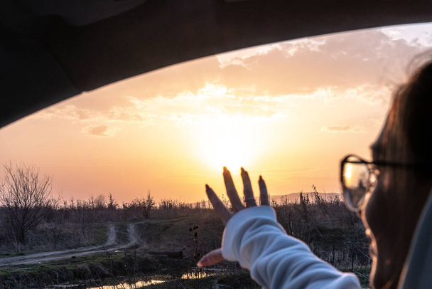 幸せな女性は日没の背景に車の中で座っている - 写真・画像