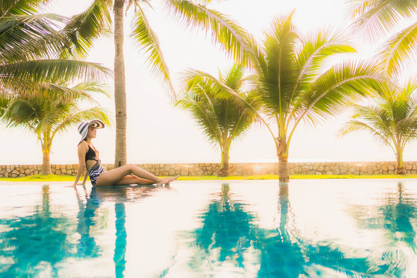 Retrato hermosa mujer asiática joven relajarse alrededor de la piscina al aire libre en el complejo hotelero con palmera al atardecer o al amanecer para vacaciones de ocio - Foto, imagen