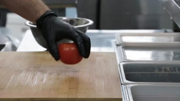 The cook cuts a red tomato with a sharp knife on a cutting board - Materiał filmowy, wideo