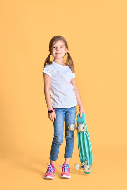 Stylish funny girl wearing white t-shirt, blue jeans and sneakers, holding skateboard over yellow background - Φωτογραφία, εικόνα