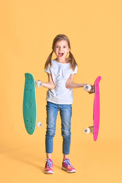 Stylish funny girl wearing white t-shirt, blue jeans and sneakers, holding two skateboard over yellow background - Fotoğraf, Görsel