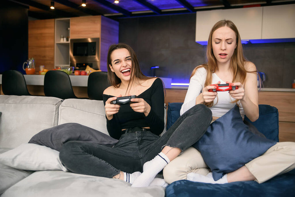 Zwei Freundinnen spielen zu Hause leidenschaftlich Computerspiele, während sie unter Quarantäne stehen. Weltweite Pandemie-Isolation zu Hause. Zeit genießen, um Freizeit zu verbringen. - Foto, Bild