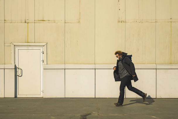 muž v masce běh sám na ulici továrna bílá zeď a dveře jednoduché pozadí průmyslu prostor - Fotografie, Obrázek