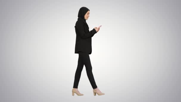 vrouw in hijab met behulp van mobiele telefoon lopen op gradiënt achtergrond. - Video