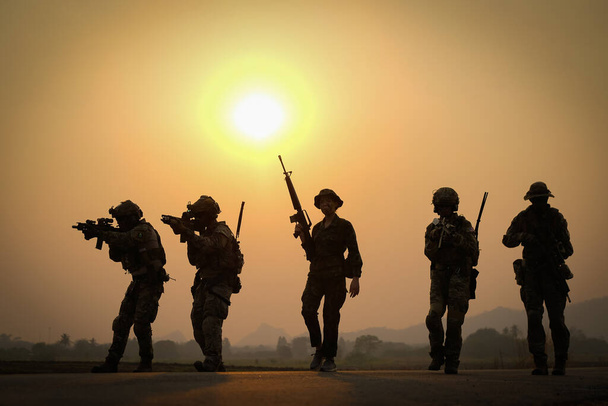 Силует групи солдатів тримає зброю і йде по дорозі з заходом сонця в спину
. - Фото, зображення