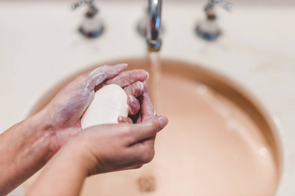 flattening the curve through hygiene against pandemic outbreaks like covid-19, woman washing her hands in the bathroom holidng soap bar shot at shallow depth of field - Фото, зображення