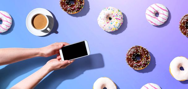 Person using a smartphone with donuts - Valokuva, kuva