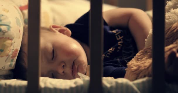 A baba esténként felébred a bölcsőben és sír. A lámpa meleg fénye a gyermekre esik. Közelkép - Felvétel, videó