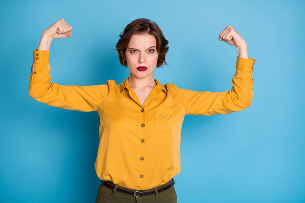 Girls power. Photo of pretty serious lady hold raise biceps two hands showing perfect biceps after gym training wear yellow shirt green pants isolated bright blue color background - Photo, Image